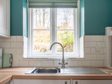 A kitchen sink under a window with blue walls and white tiles at Greenhowes Graythwaite near Hawkshead