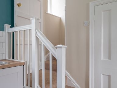 A stairway with carpeted steps and white painted wooden handrails next to a kitchen counter at Greenhowes in Graythwaite near Hawkshead