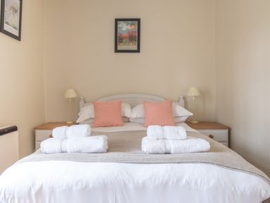 A bedroom with a double bed two bedside tables with lamps and rolled towels on the bed at Greenhowes Graythwaite near Hawkshead