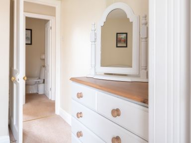 A hallway with a white dresser with a mirror and an open door leading to a bathroom at Greenhowes Graythwaite near Hawkshead