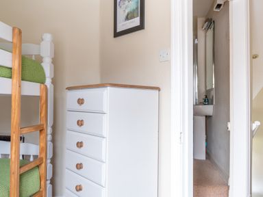 A bedroom corner with a white wooden chest of drawers and a bunk bed with green bedding at Greenhowes in Graythwaite near Hawkshead