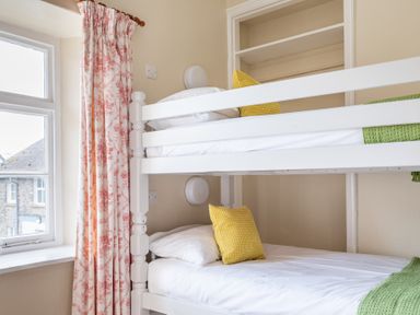 A bedroom with a white bunk bed yellow pillows and floral curtains at Greenhowes in Graythwaite near Hawkshead