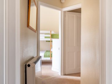 A hallway with a wall heater and a mirror leading to a bedroom with bunk beds at Greenhowes Graythwaite near Hawkshead