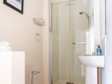 A bathroom with a glass shower enclosure a wall-mounted sink with a soap dispenser a towel ring and a metal basket on the wall at Greenhowes Graythwaite near Hawkshead