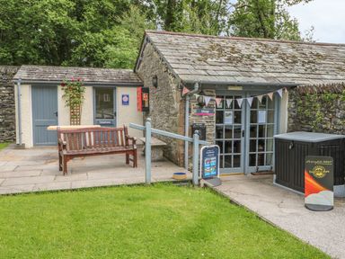 A stone building with a shop entrance and a bench outside near a telephone booth at Jubilee in Graythwaite near Hawkshead