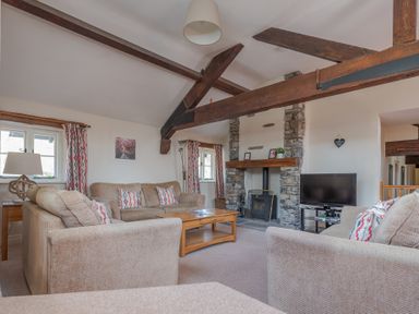 A living room with sofas coffee table stone fireplace and wooden ceiling beams at Lords Leap in Graythwaite near Hawkshead