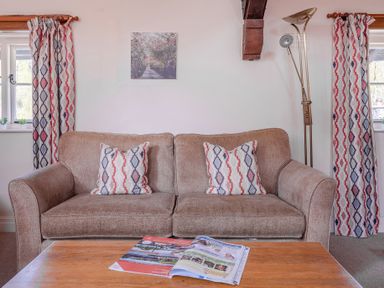 A living room with a brown sofa and patterned cushions next to windows with matching curtains and a coffee table with magazines at Lords Leap Graythwaite near Hawkshead