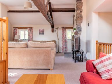 A living room with beige and red sofas exposed wooden beams and a stone fireplace at Lords Leap Graythwaite near Hawkshead