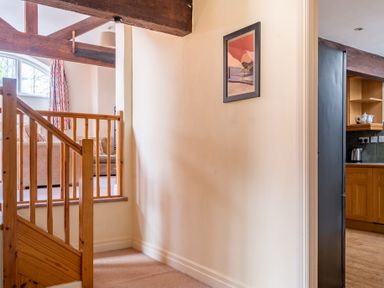 A staircase with wooden railing leading to a living room with a sofa and curtains and a kitchen with wooden cabinets and appliances at Lords Leap in Graythwaite near Hawkshead
