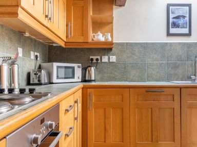 A kitchen with wooden cabinets a countertop microwave toaster kettle and a framed picture on the wall at Lords Leap in Graythwaite near Hawkshead