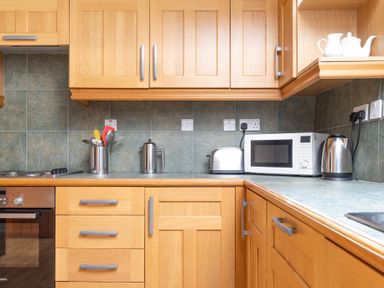 A kitchen with wooden cabinets a microwave toaster kettle and cooking utensils at Lords Leap Graythwaite near Hawkshead