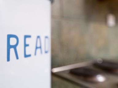 A close up of a white object with blue letters reading read and a blurred background with tiles and part of a stove