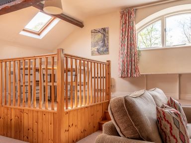 An upstairs seating area with wooden railing a skylight window patterned curtains and beige sofa with cushions at Lords Leap Graythwaite near Hawkshead