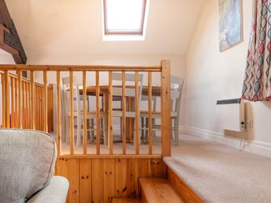 A dining area with wooden table and chairs viewed from stairs with wooden railing at Lords Leap in Graythwaite near Hawkshead