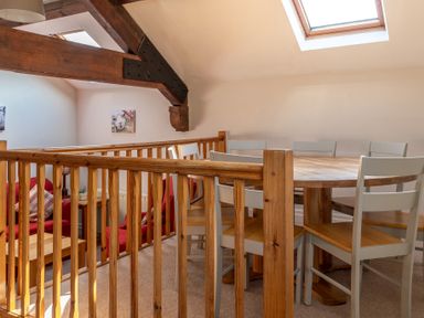 A dining area with a round wooden table and chairs near a wooden railing under a skylight at Lords Leap Graythwaite near Hawkshead