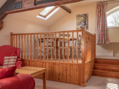 A sitting area with red chairs and a wooden table next to a raised dining area with wooden chairs and a table under a skylight at Lords Leap in Graythwaite near Hawkshead