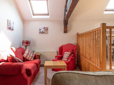 A sitting area with a red sofa and armchair with cushions a wooden coffee table and railing at Lord's Leap in Graythwaite near Hawkshead