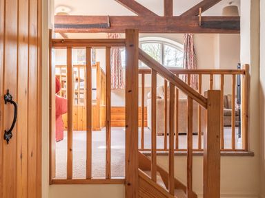 A wooden stair railing and gate opening to a living area with chairs and a window at Lords Leap in Graythwaite near Hawkshead
