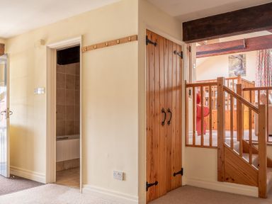 An interior view showing a carpeted hallway with a wooden door under stairs a tiled bathroom door and a wooden staircase railing leading to a living area at Lords Leap in Graythwaite near Hawkshead