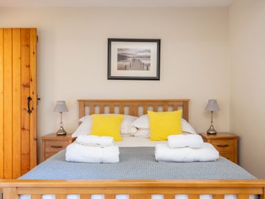 A bedroom with a wooden bed frame yellow pillows white towels bedside tables and lamps Lord's Leap Graythwaite near Hawkshead