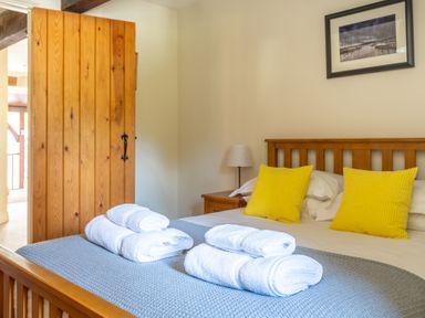 A bedroom with a wooden bed with yellow pillows white towels on a blue blanket and a wooden door at Lords Leap in Graythwaite near Hawkshead