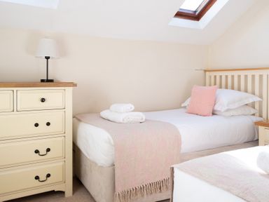 A bedroom with two single beds with pink throws and pillows a cream chest of drawers and lamp at Lords Leap in Graythwaite near Hawkshead
