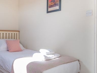 A single bed with white linen and a pink cushion and blanket with folded white towels on top at Lords Leap in Graythwaite near Hawkshead