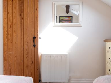 A wooden door next to a white heater with a mirror above reflecting a framed picture and a sloped ceiling at Lords Leap in Graythwaite near Hawkshead