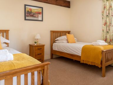A bedroom with two single wooden beds yellow blankets a wooden bedside table lamp and floral curtains at Lords Leap Graythwaite near Hawkshead