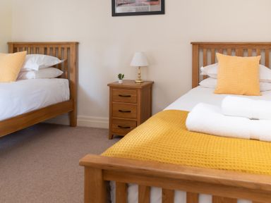 A bedroom with two wooden beds with yellow pillows and blankets and a wooden nightstand with a lamp and small plant at Lord's Leap in Graythwaite near Hawkshead