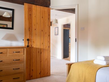 A bedroom with a wooden dresser an open wooden door a bed with a yellow blanket and white towels at Lords Leap in Graythwaite near Hawkshead