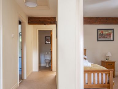 A hallway leading to a bathroom with a toilet and a bedroom with a wooden bed and nightstand at Lords Leap Graythwaite near Hawkshead