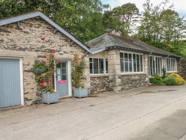 A stone building with blue doors and window frames with plants and flowers outside at Bassicks Hawkshead
