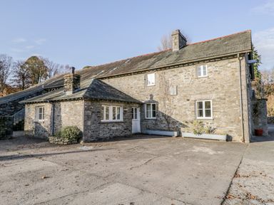 Stone house with multiple windows chimneys and planters on a concrete driveway at Bassicks in Hawkshead