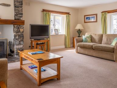 A living room with a beige sofa a wooden coffee table a flat screen tv on a stand and stone fireplace at Bassicks in Hawkshead