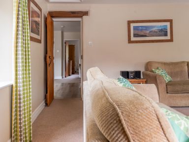 A living room with beige sofas patterned cushions a wooden door and framed pictures on the wall at Bassicks in Hawkshead