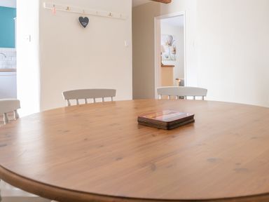 A wooden dining table with a stack of coasters and white chairs in a dining area at Bassicks Hawkshead
