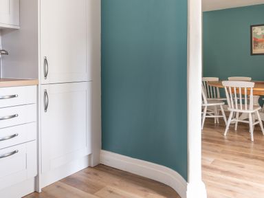 A kitchen with white cabinets next to a dining area with a wooden table and white chairs at Bassicks in Hawkshead