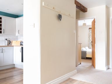 A hallway with coat hooks on the wall leading to a kitchen and a bedroom at Bassicks in Hawkshead