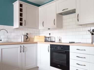 A kitchen with white cabinets a black oven a toaster a kettle and a bread box at Bassicks in Hawkshead
