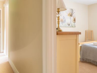 A hallway leading to a bedroom with a lamp on a dresser a chair and a bed with a gray throw at Bassicks Hawkshead