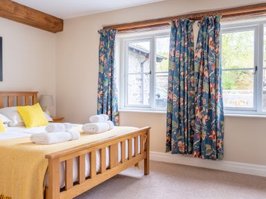 A bedroom with a wooden bed with yellow cushions and folded white towels on the bed at Bassicks Hawkshead