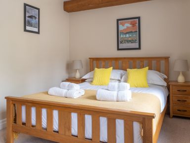 A bedroom with a wooden bed frame yellow pillows folded towels bedside tables and lamps at Bassicks in Hawkshead
