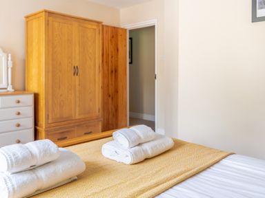 A bedroom with a bed with folded white towels on a yellow blanket and wooden wardrobe Bassicks Hawkshead