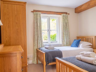 A bedroom with two single wooden beds and a wooden wardrobe near a window with curtains at Bassicks Hawkshead