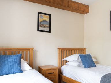 A bedroom with two single wooden beds a wooden nightstand and a framed picture on the wall at Bassicks in Hawkshead