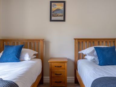 A bedroom with two single wooden beds with blue pillows and a three drawer wooden nightstand in between at Bassicks in Hawkshead