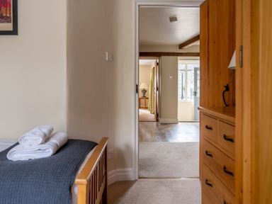 A bedroom with a wooden bed and dresser leading to a hallway with a lamp and a door at Bassicks in Hawkshead
