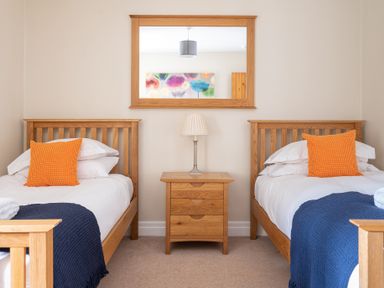 A bedroom with two single wooden beds blue throws and orange pillows at Bassicks in Hawkshead