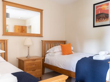 A bedroom with two single wooden beds a wooden bedside table with lamp a large mirror and a framed picture at Bassicks in Hawkshead